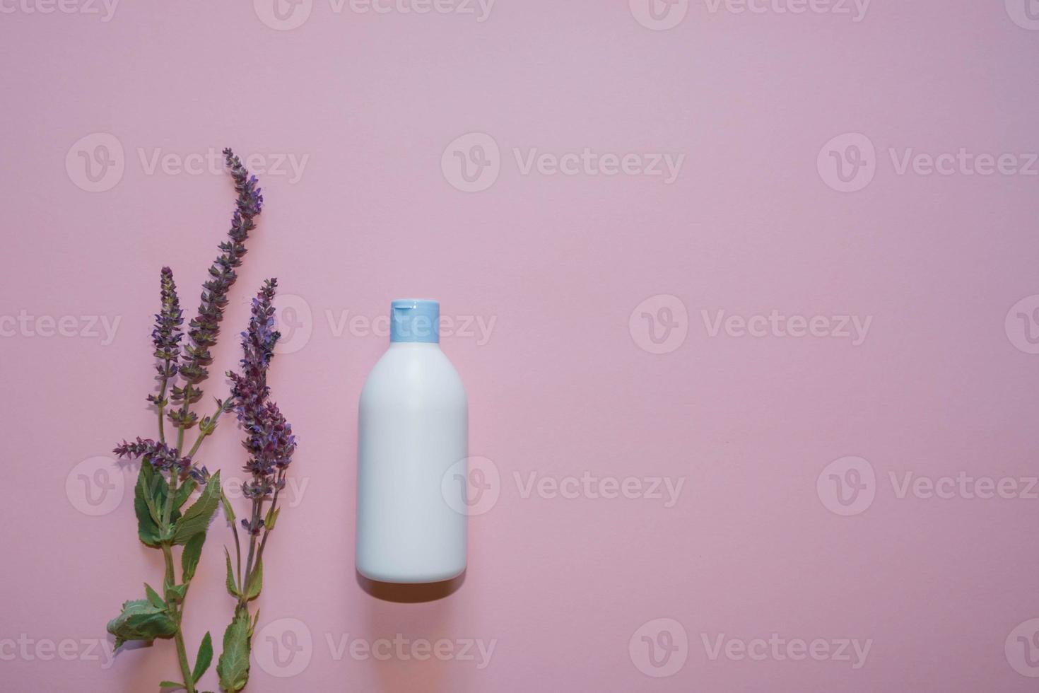 White plastic bottle with lavender flowers on a violet background. Copy space. Top view photo