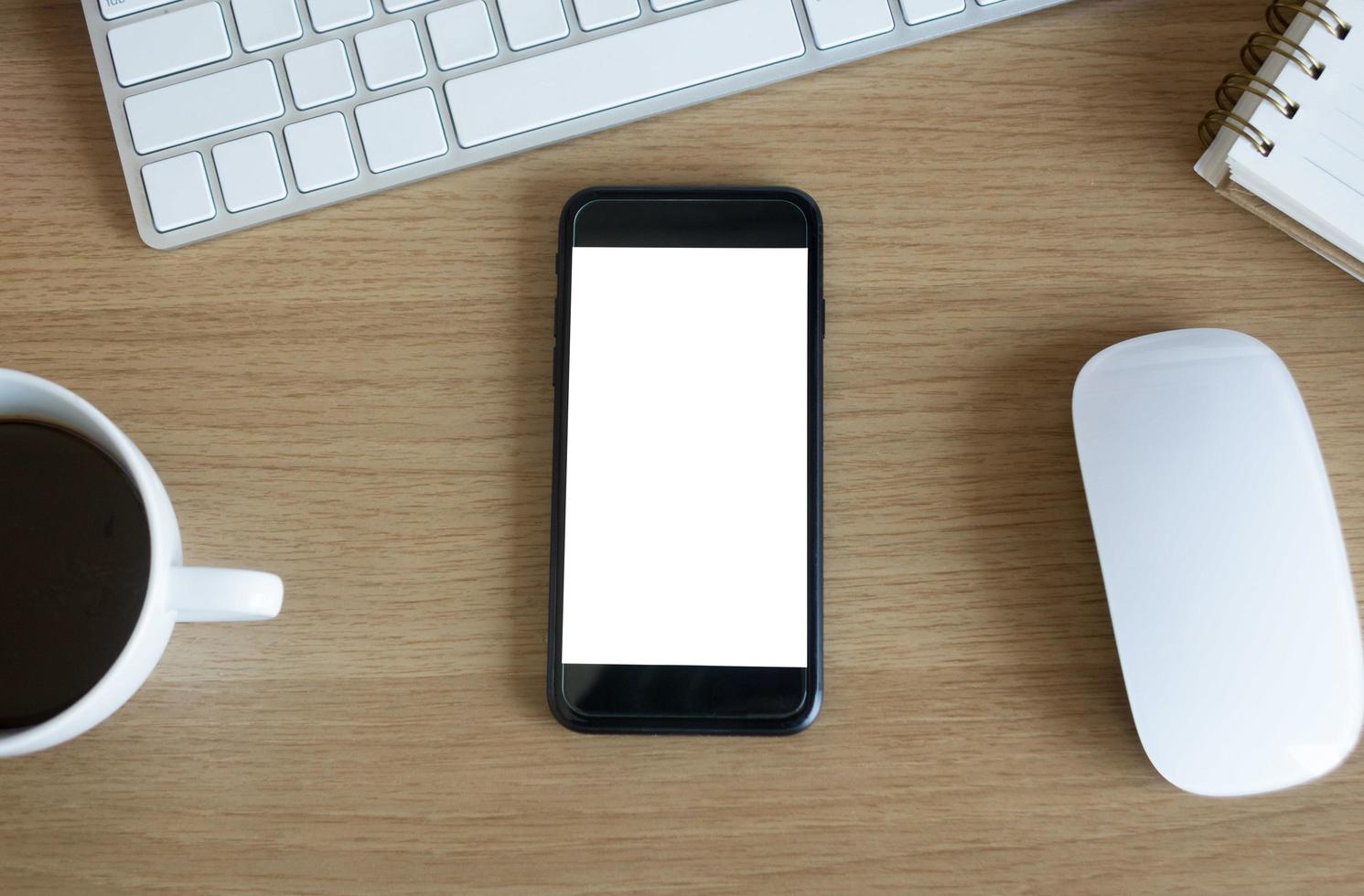 mesa de escritorio de oficina con teléfono inteligente de pantalla en blanco foto