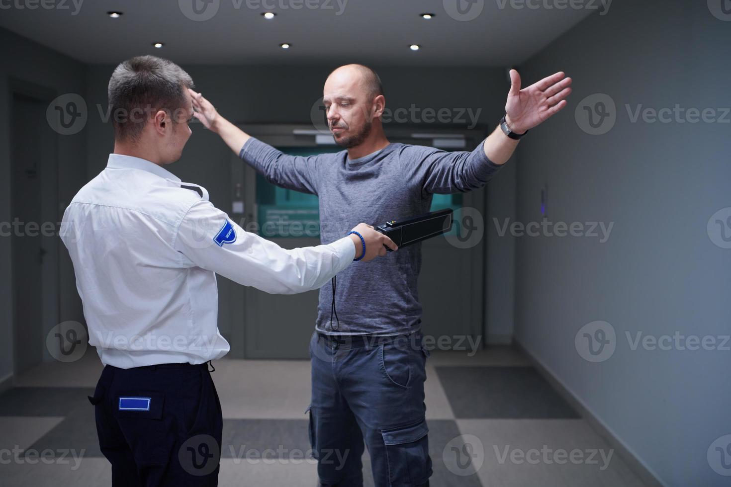 Security guard with a metal detector making body searching procedure on man photo