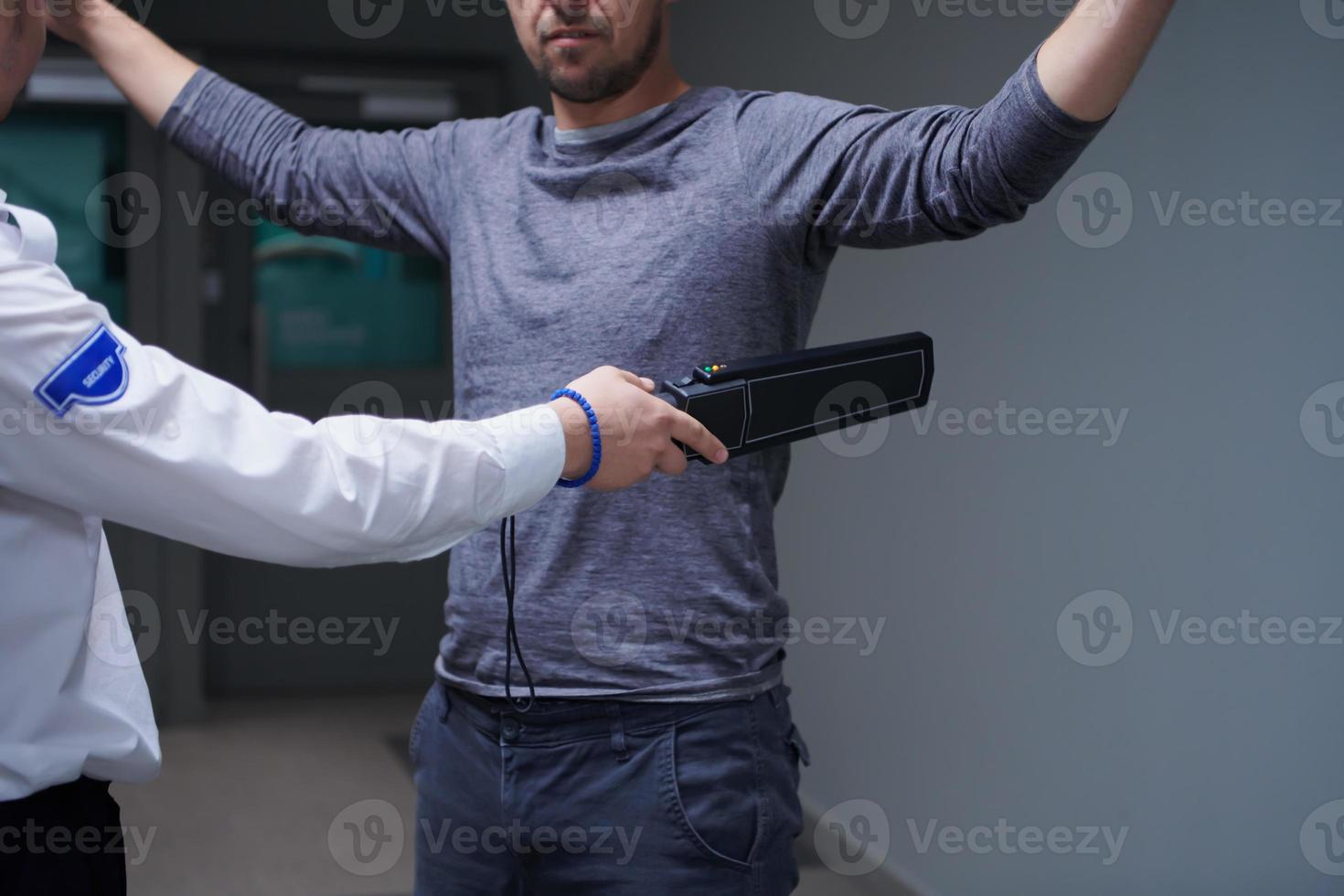 Security guard with a metal detector making body searching procedure on man photo