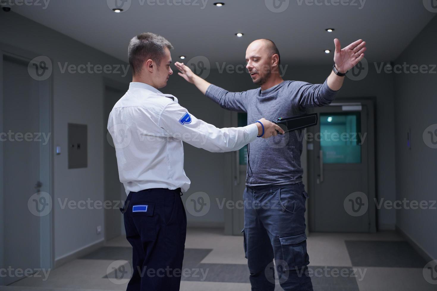 Security guard with a metal detector making body searching procedure on man photo