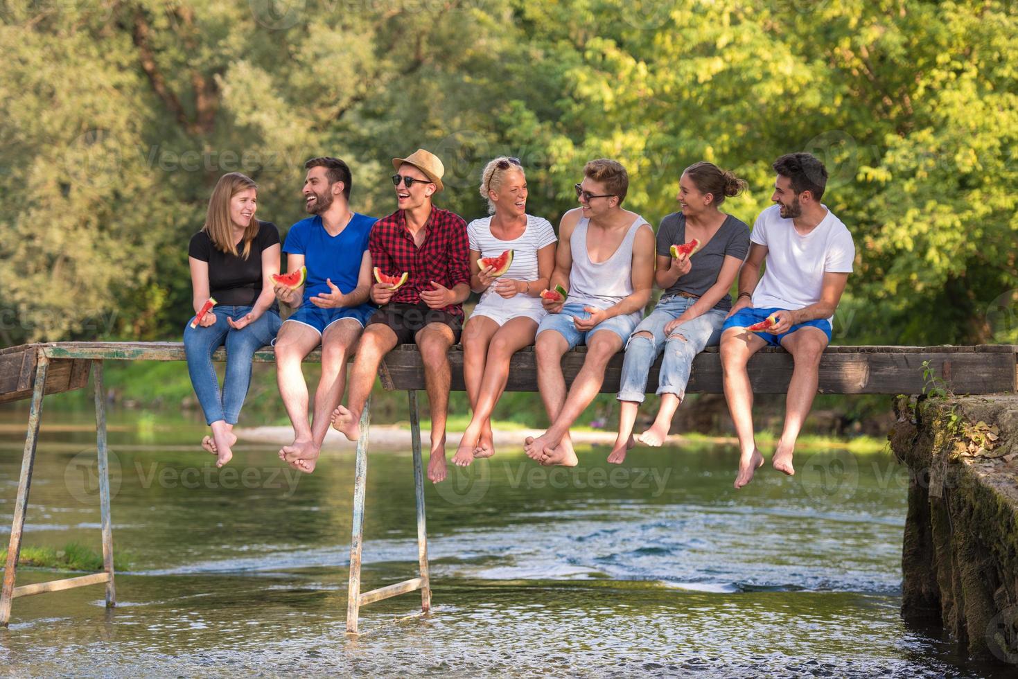 amigos disfrutando de la sandía mientras están sentados en el puente de madera foto