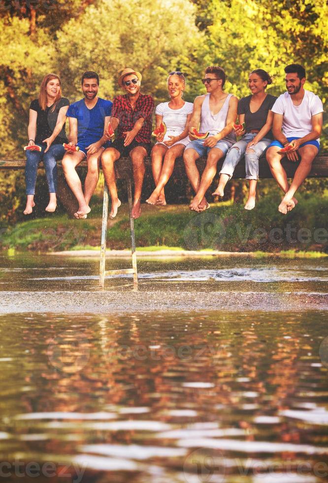 friends enjoying watermelon while sitting on the wooden bridge photo