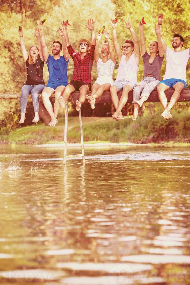 friends enjoying watermelon while sitting on the wooden bridge photo