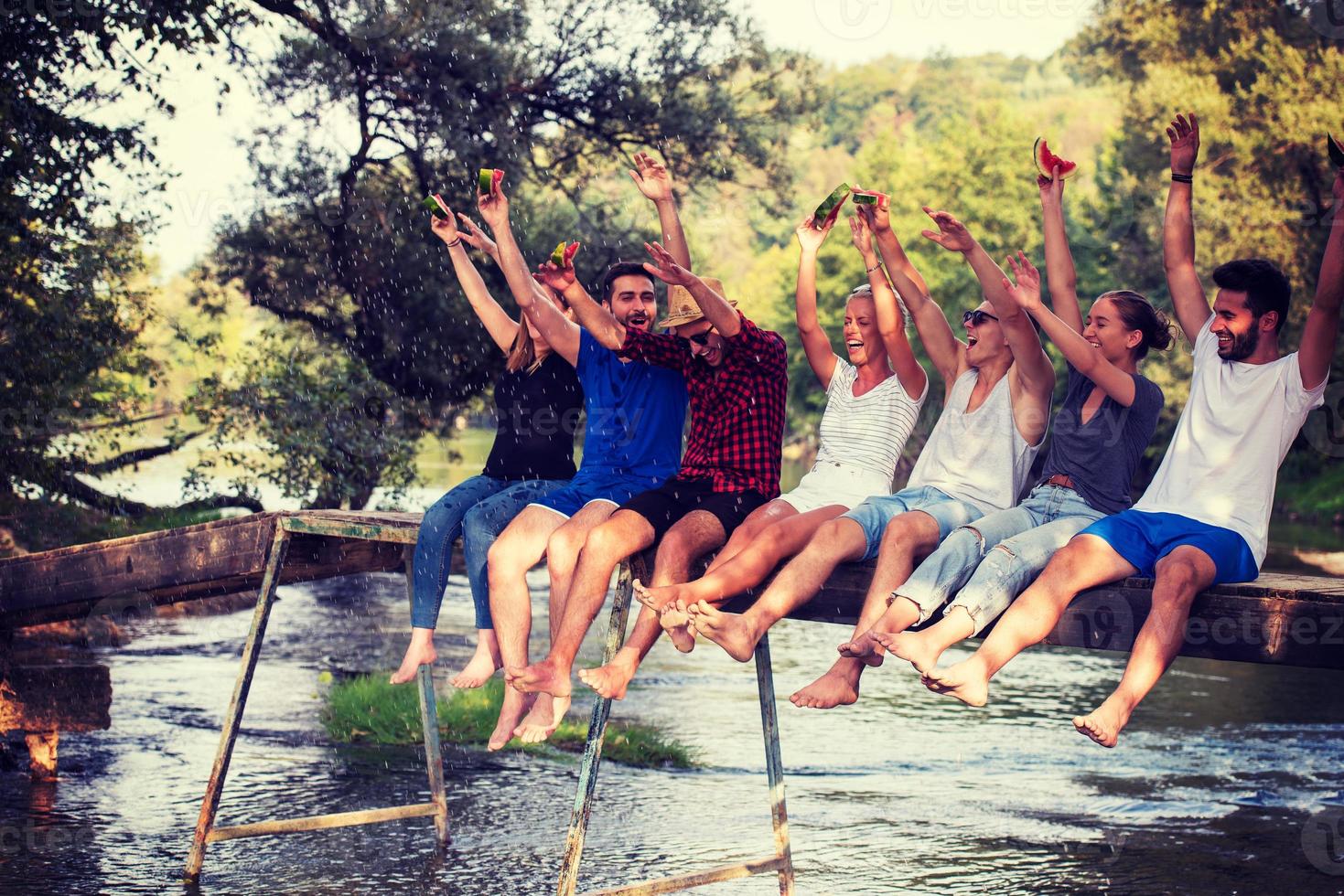 friends enjoying watermelon while sitting on the wooden bridge photo