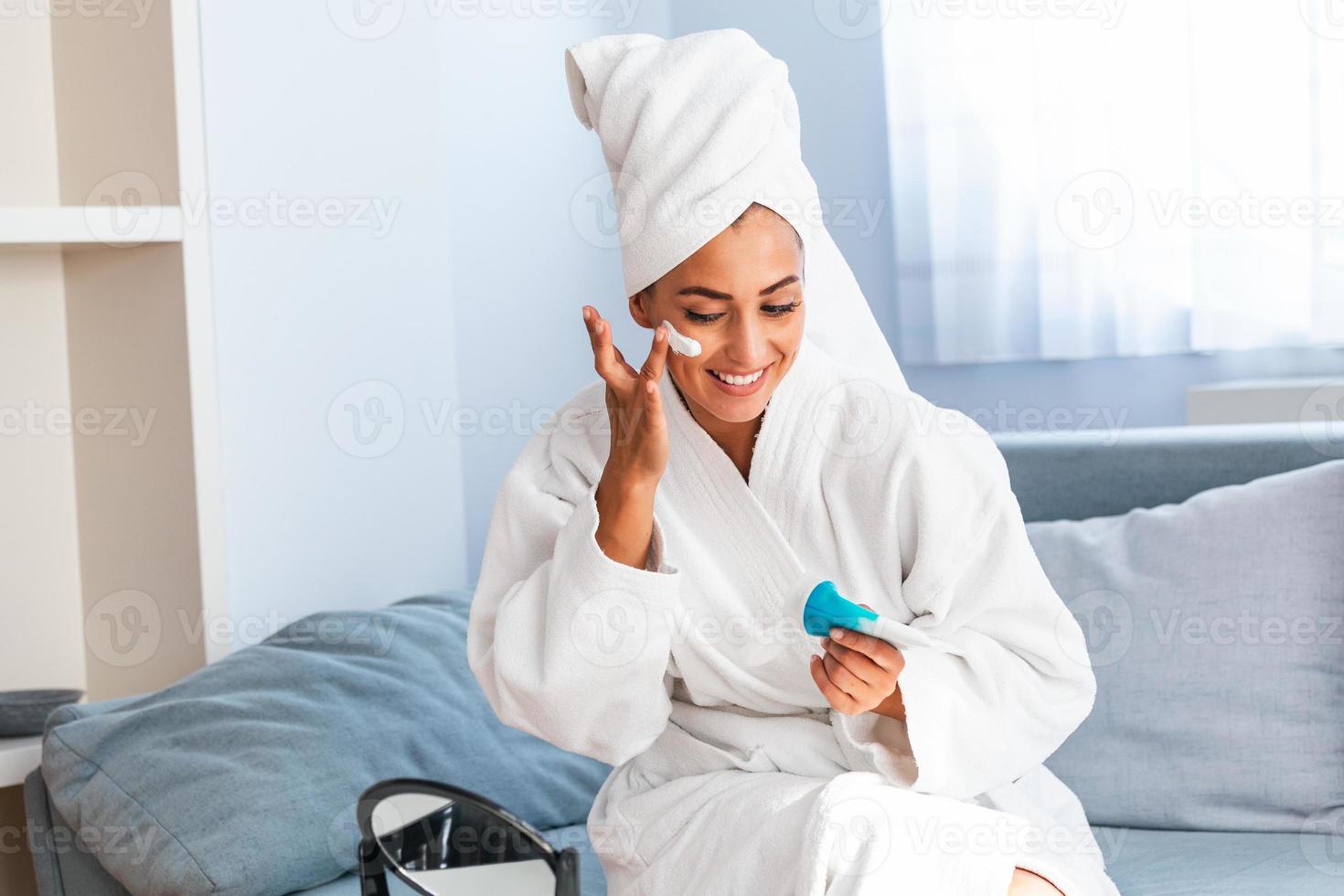 Young beautiful woman applying homemade facial mask i at home.Skin care, beauty treatments. So beautiful. Close-up of girl with beauty mask on her face looking in mirror. photo