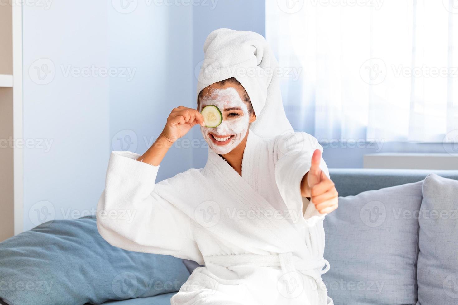 hermosa mujer joven con máscara facial en la cara sosteniendo rodajas de pepino fresco. concepto de cuidado y tratamiento de la piel, spa, belleza natural y cosmetología foto
