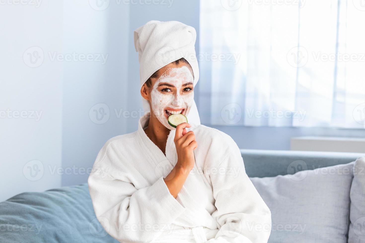 mujer con máscara facial y rodajas de pepino en las manos. bella mujer joven con máscara facial en la cara sosteniendo rodajas de pepino fresco. mujer joven con máscara facial de arcilla sosteniendo rodajas de pepino foto