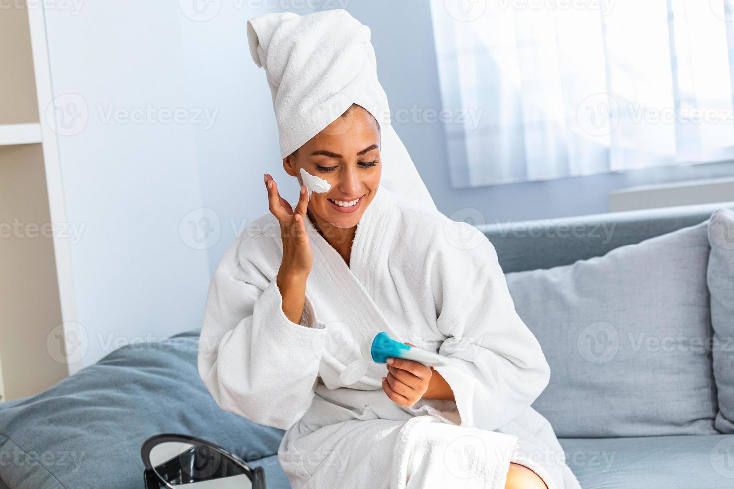 Young beautiful woman applying homemade facial mask i at home.Skin care, beauty treatments. So beautiful. Close-up of girl with beauty mask on her face looking in mirror. photo