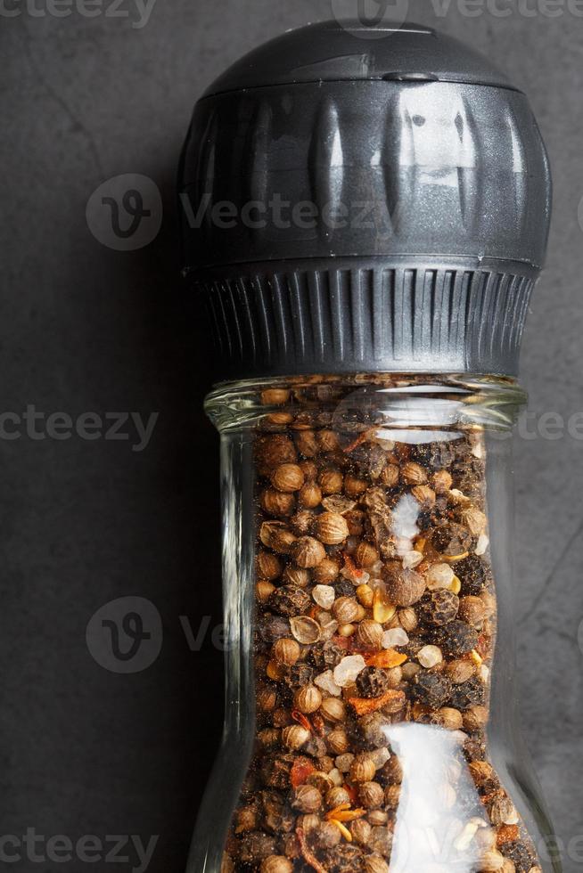 una mezcla de condimentos, especias y hierbas en un molino de vidrio sobre un fondo negro. foto