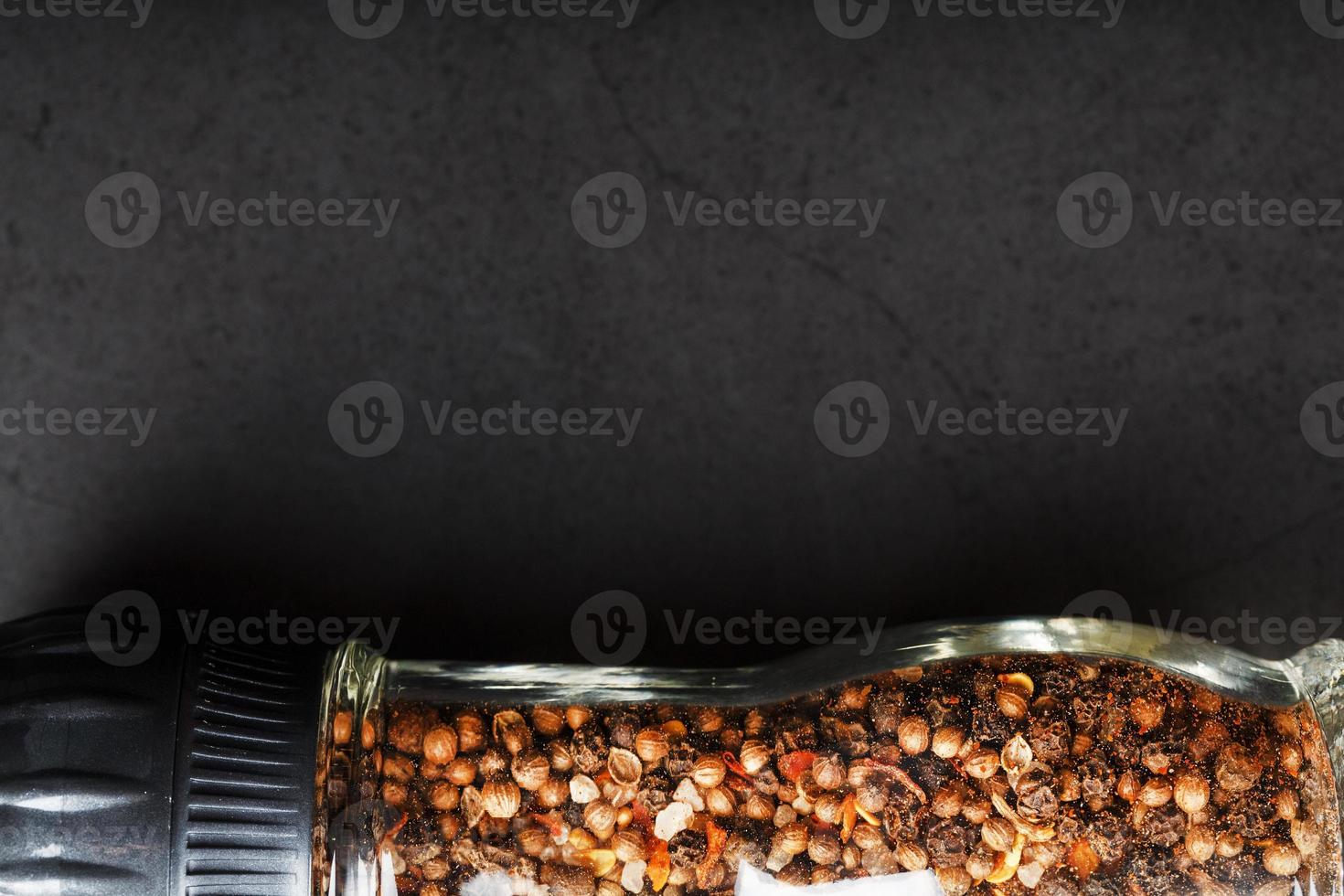 A mixture of seasonings, spices and herbs in a glass mill on a black background. photo