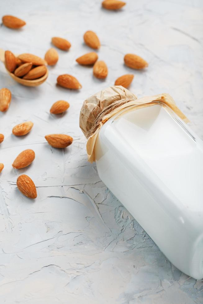 leche de almendras en una botella de vidrio sobre un fondo claro con una dispersión de semillas y una cuchara de madera. foto