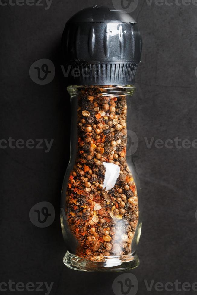 A mixture of seasonings, spices and herbs in a glass mill on a black background. photo