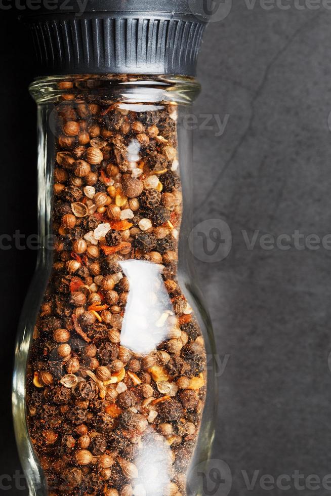Seasoning mixture in glass mill on black background photo