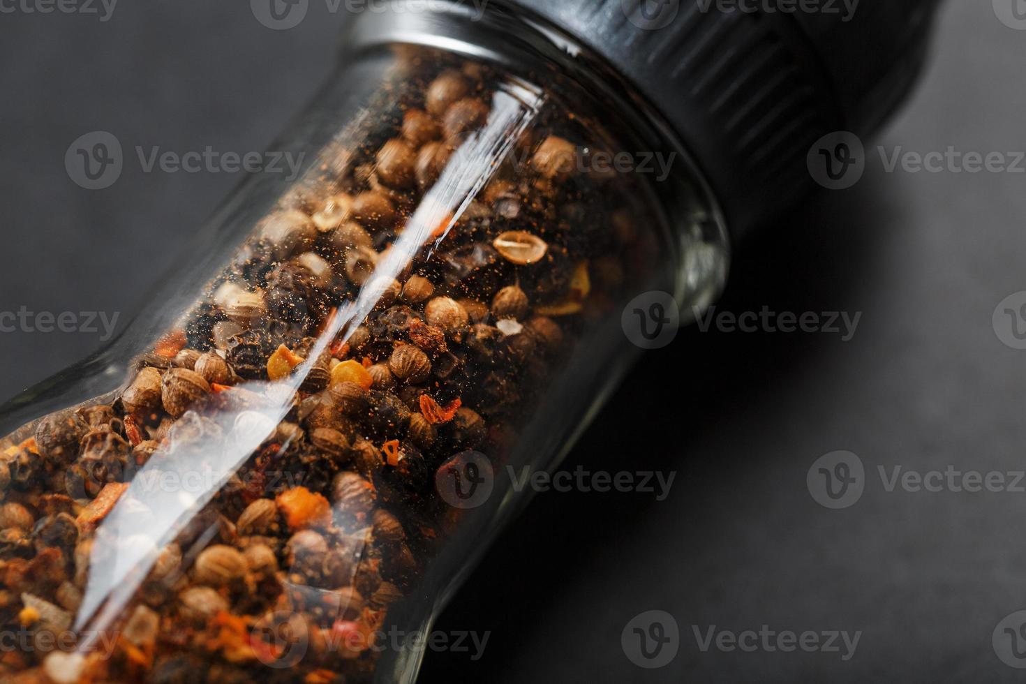 A mixture of seasonings, spices and herbs in a glass mill on a black background. photo