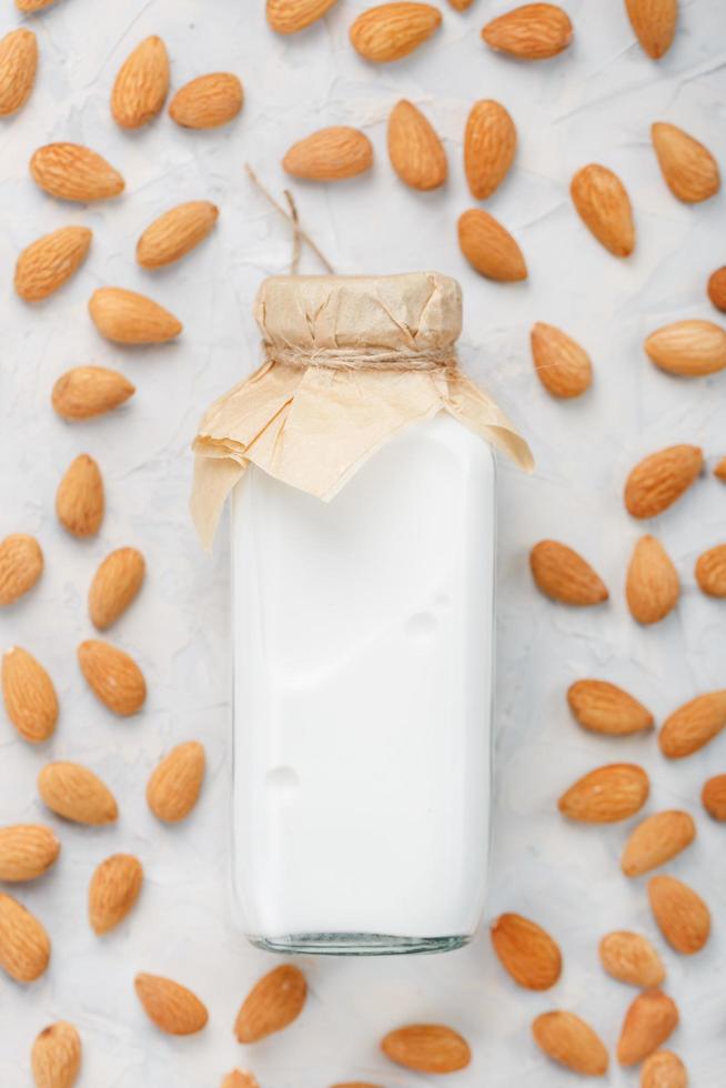 Vegan Milk from organic almonds in a glass bottle around a scattering of seeds on a light background. photo