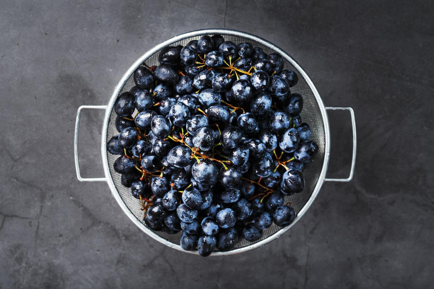 Ripe black grapes in a metal bowl on a black background. photo