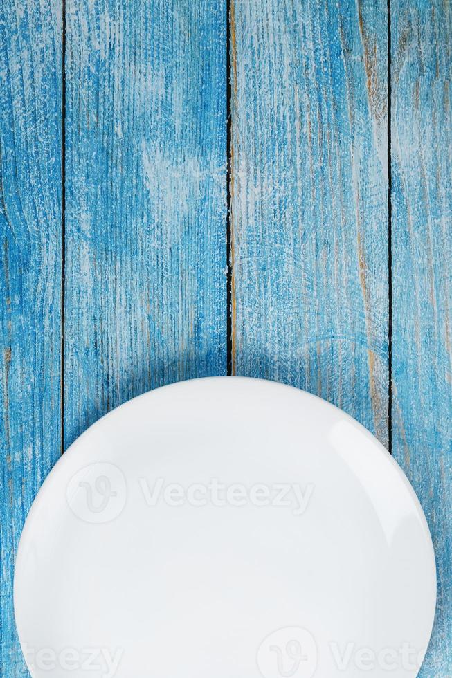 An empty round white plate on a blue wooden table. photo