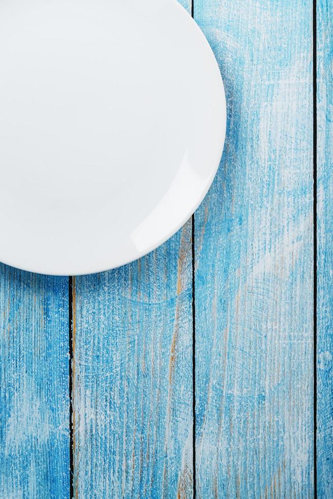 un plato blanco redondo vacío sobre una mesa de madera azul. foto