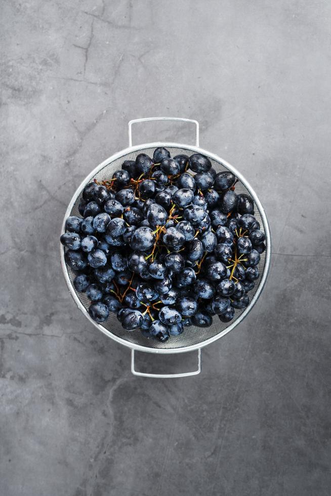 uvas negras maduras en un recipiente de metal sobre un fondo negro. foto