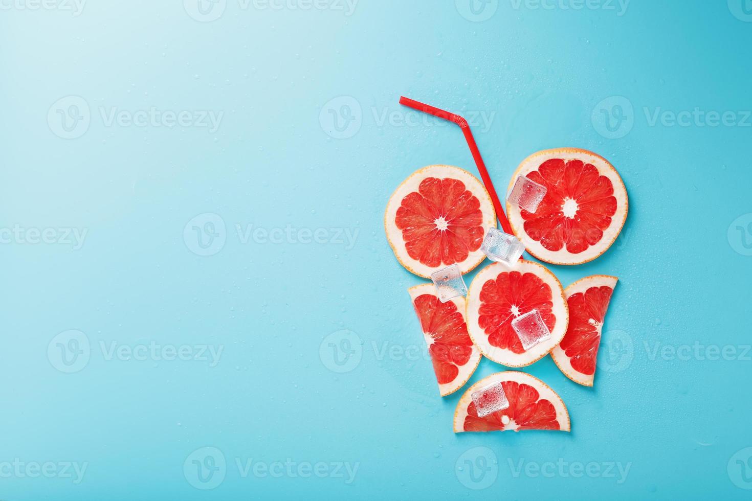 A composition of grapefruit slices and ice cubes with a straw on a blue background in the form of a refreshing drink. photo