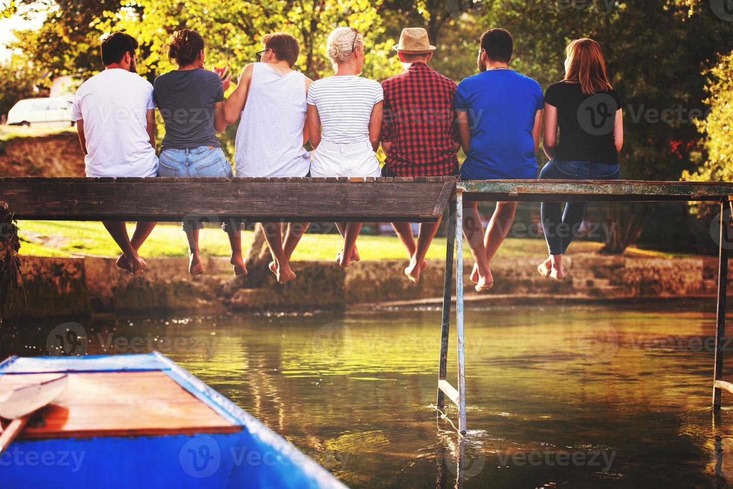 vista trasera de amigos disfrutando de sandía mientras están sentados en el puente de madera foto