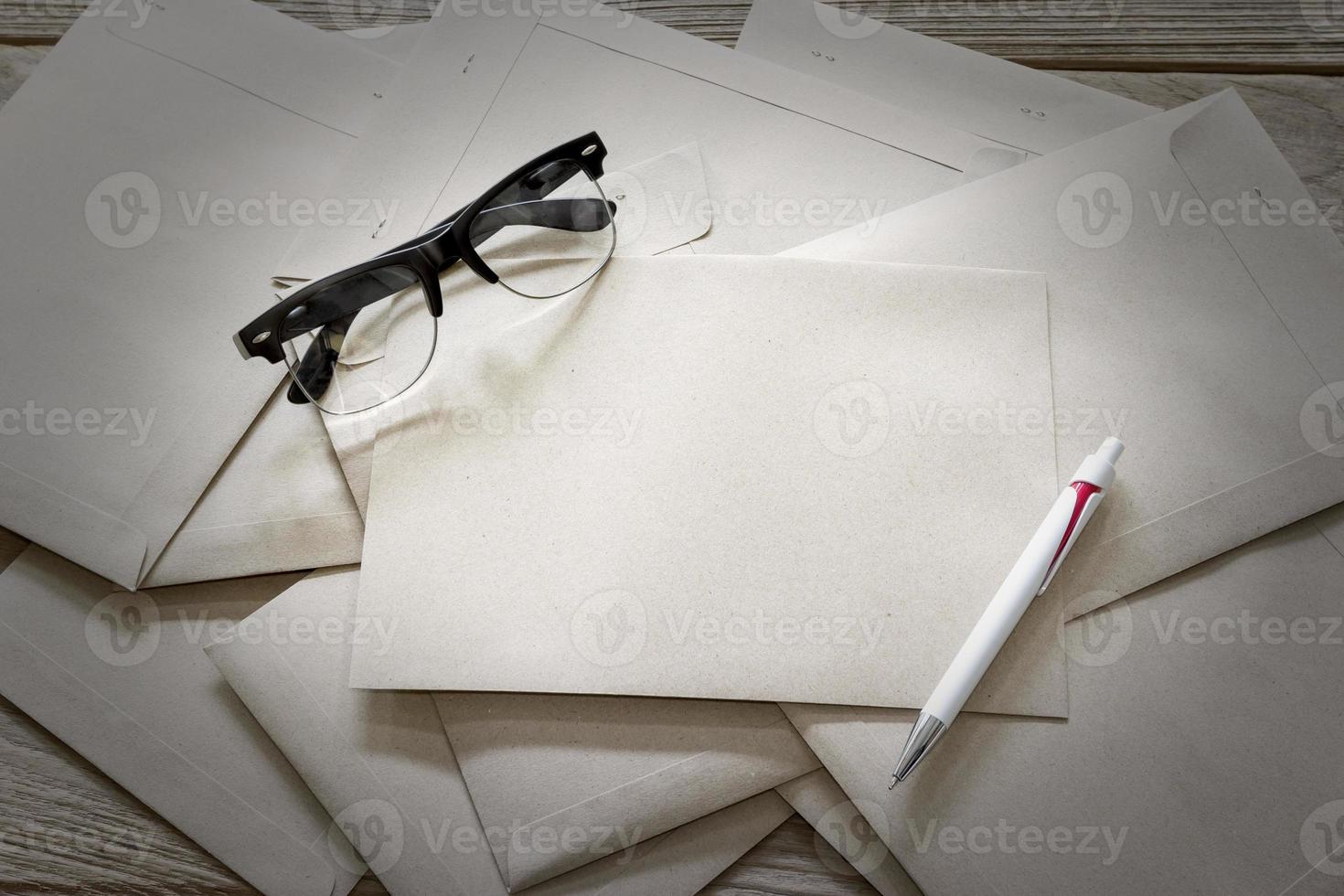 sobre de carta marrón con gafas y bolígrafo sobre mesa de madera foto