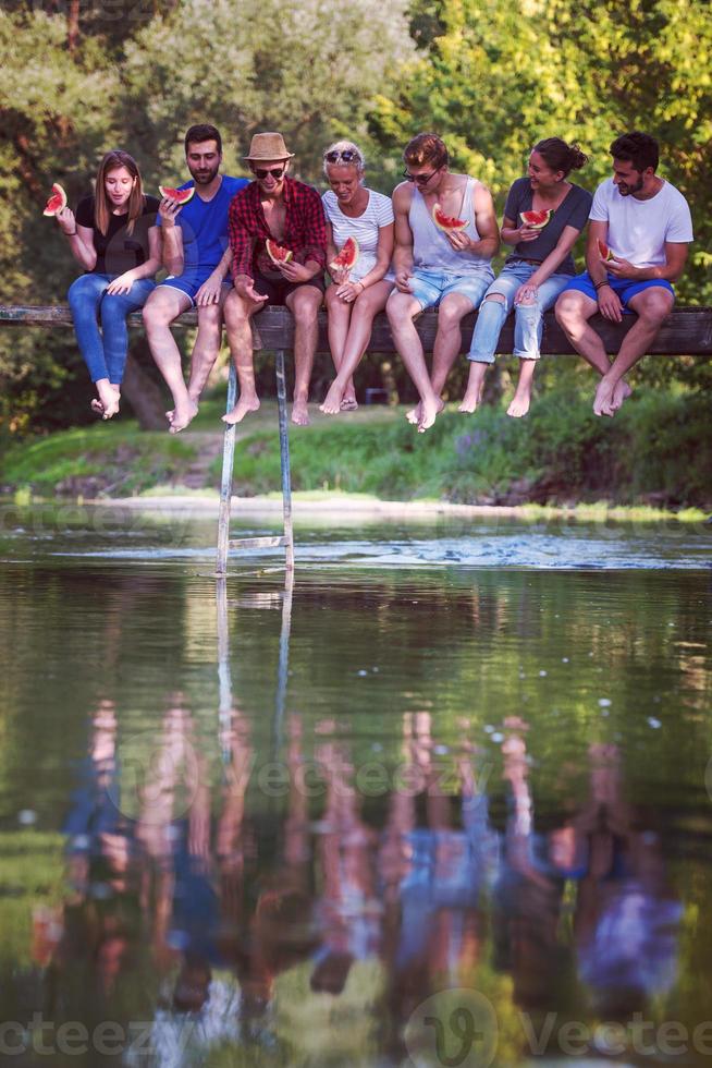 amigos disfrutando de la sandía mientras están sentados en el puente de madera foto