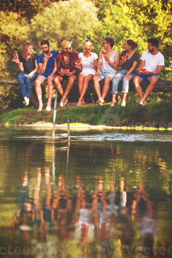 friends enjoying watermelon while sitting on the wooden bridge photo