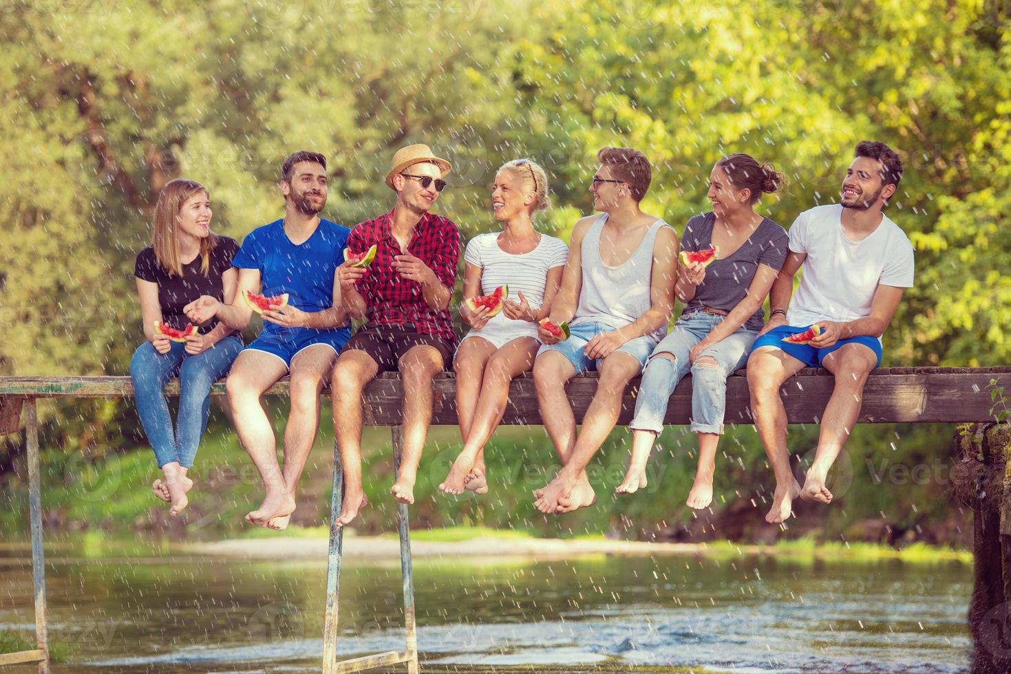 friends enjoying watermelon while sitting on the wooden bridge photo