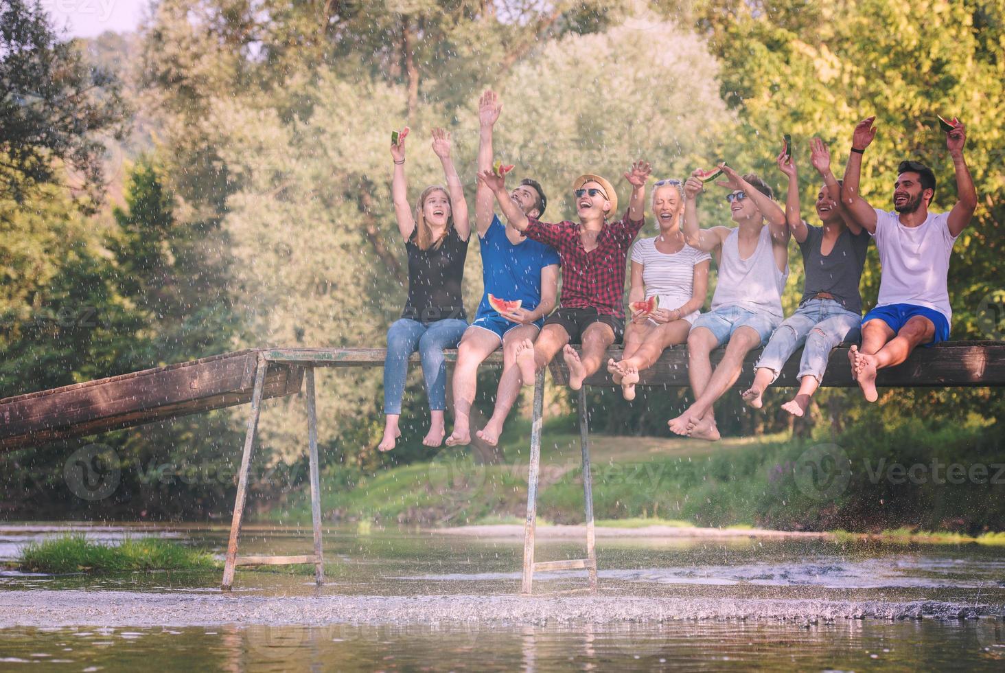 amigos disfrutando de la sandía mientras están sentados en el puente de madera foto