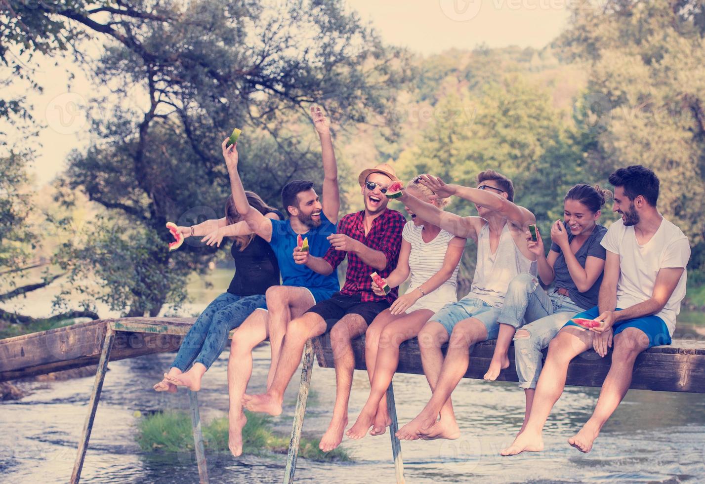 amigos disfrutando de la sandía mientras están sentados en el puente de madera foto