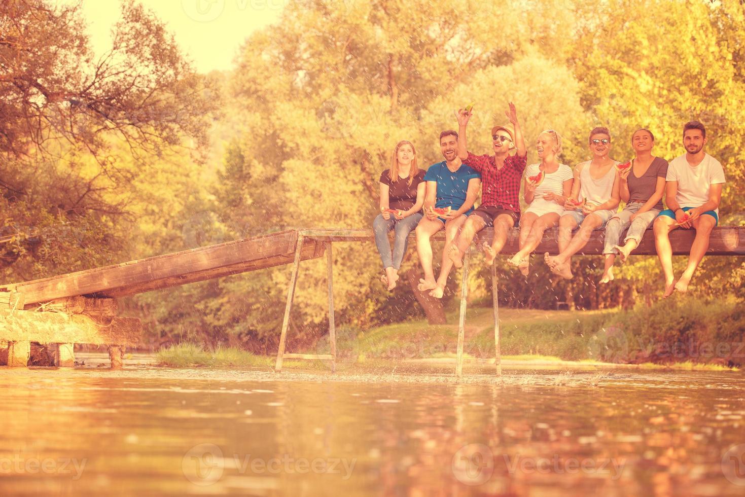 friends enjoying watermelon while sitting on the wooden bridge photo