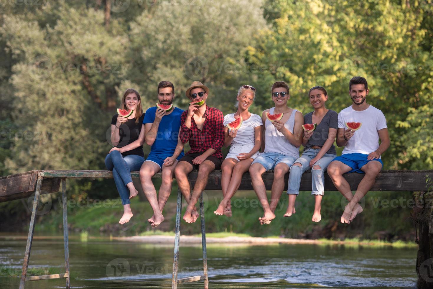 friends enjoying watermelon while sitting on the wooden bridge photo