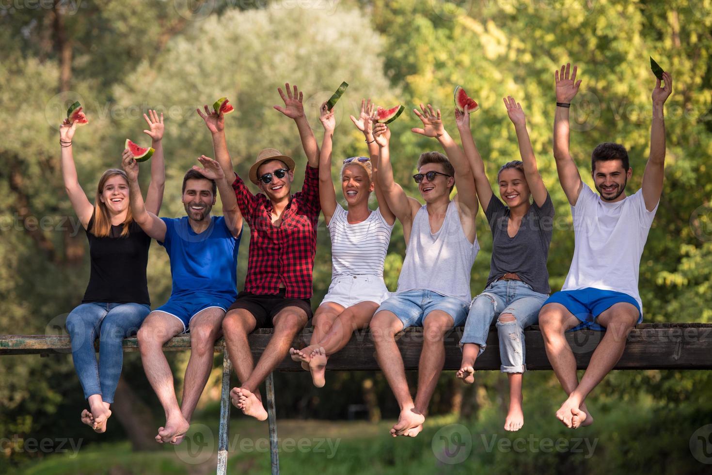 friends enjoying watermelon while sitting on the wooden bridge photo