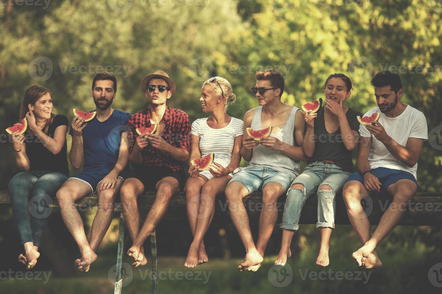 friends enjoying watermelon while sitting on the wooden bridge photo