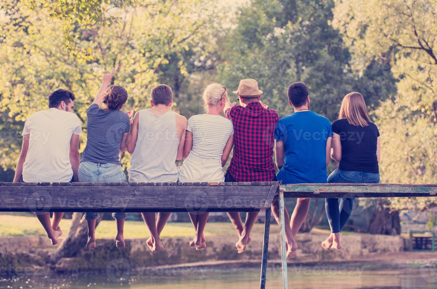 vista trasera de amigos disfrutando de sandía mientras están sentados en el puente de madera foto