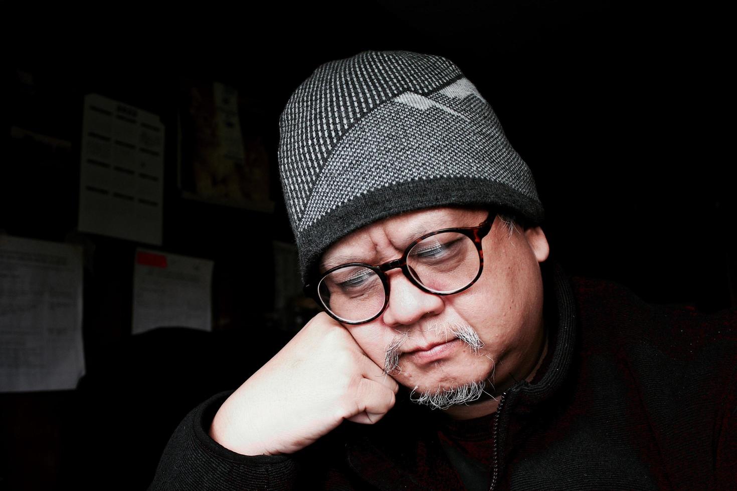 Bearded Asian man in black jacket and knitted hat. Working in a dark room and thinking to work photo