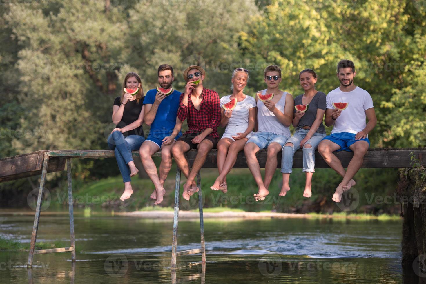 friends enjoying watermelon while sitting on the wooden bridge photo