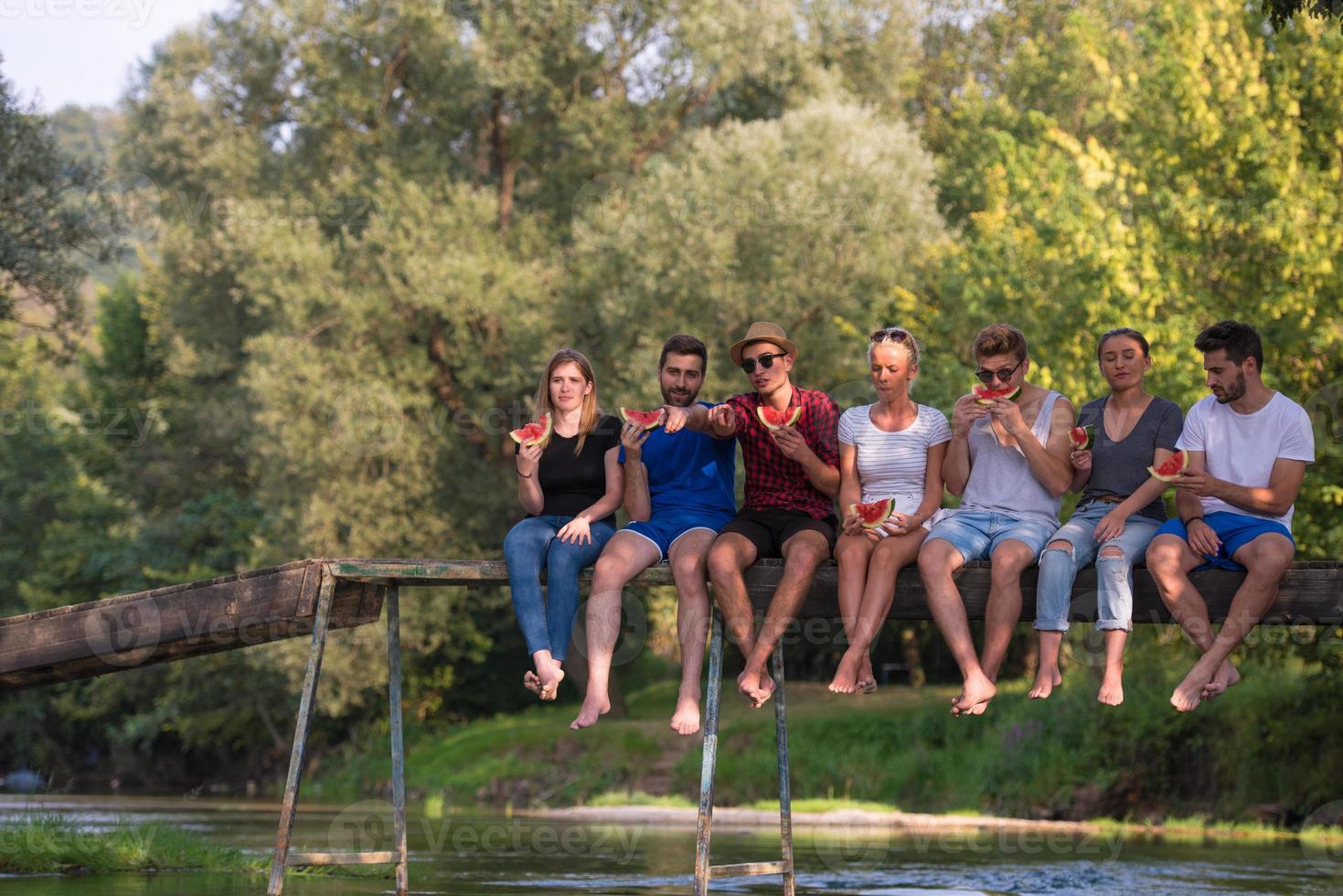 amigos disfrutando de la sandía mientras están sentados en el puente de madera foto