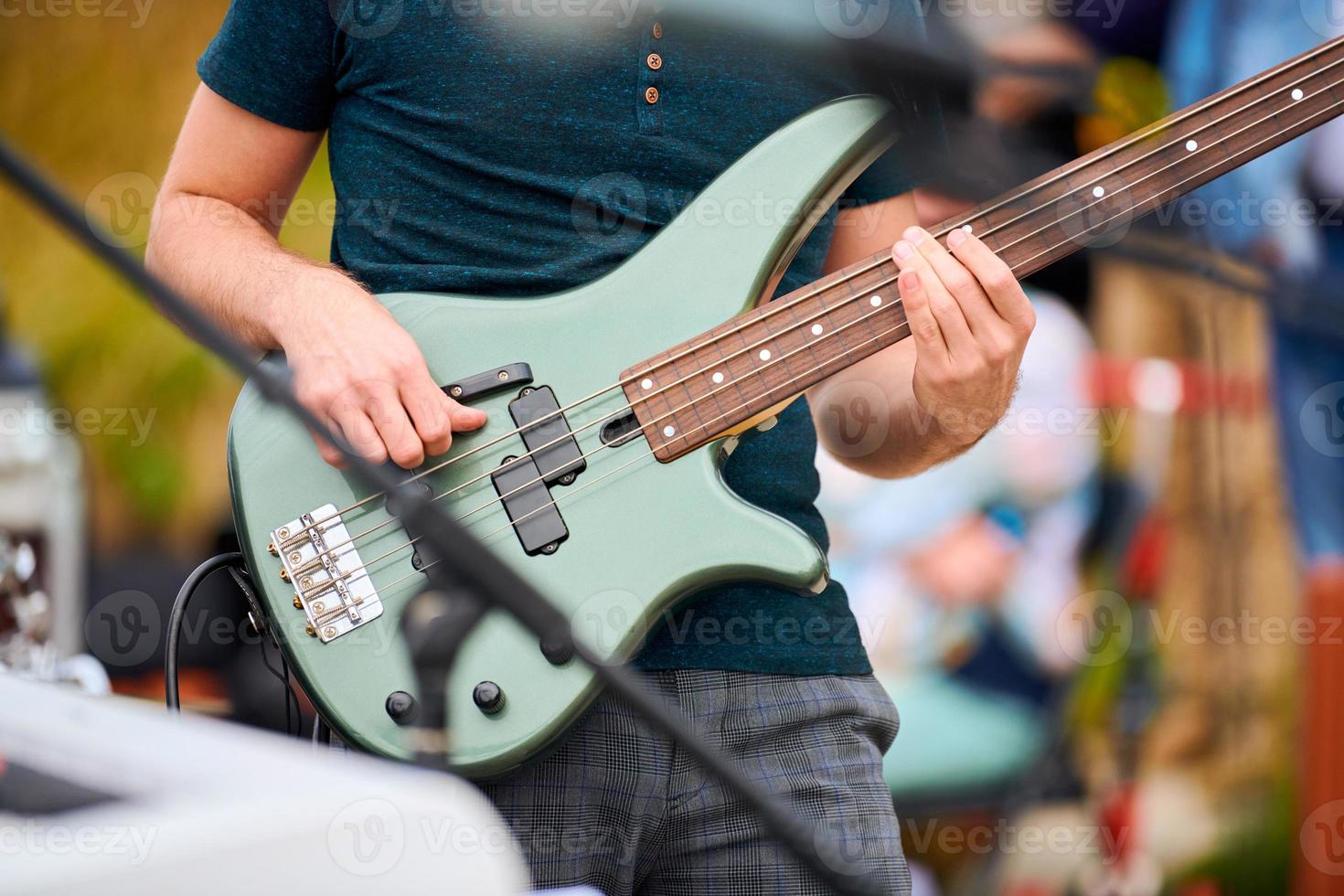 Bass guitar player hands, musician bassist playing green bass electric guitar on concert stage live photo