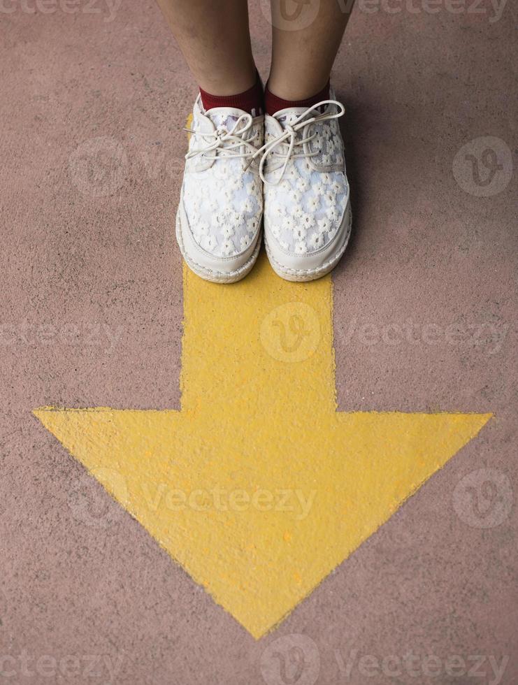 Feet and arrows on road. Yellow straight arrow sign and white shoes. Straight direction concept. Journey concept photo