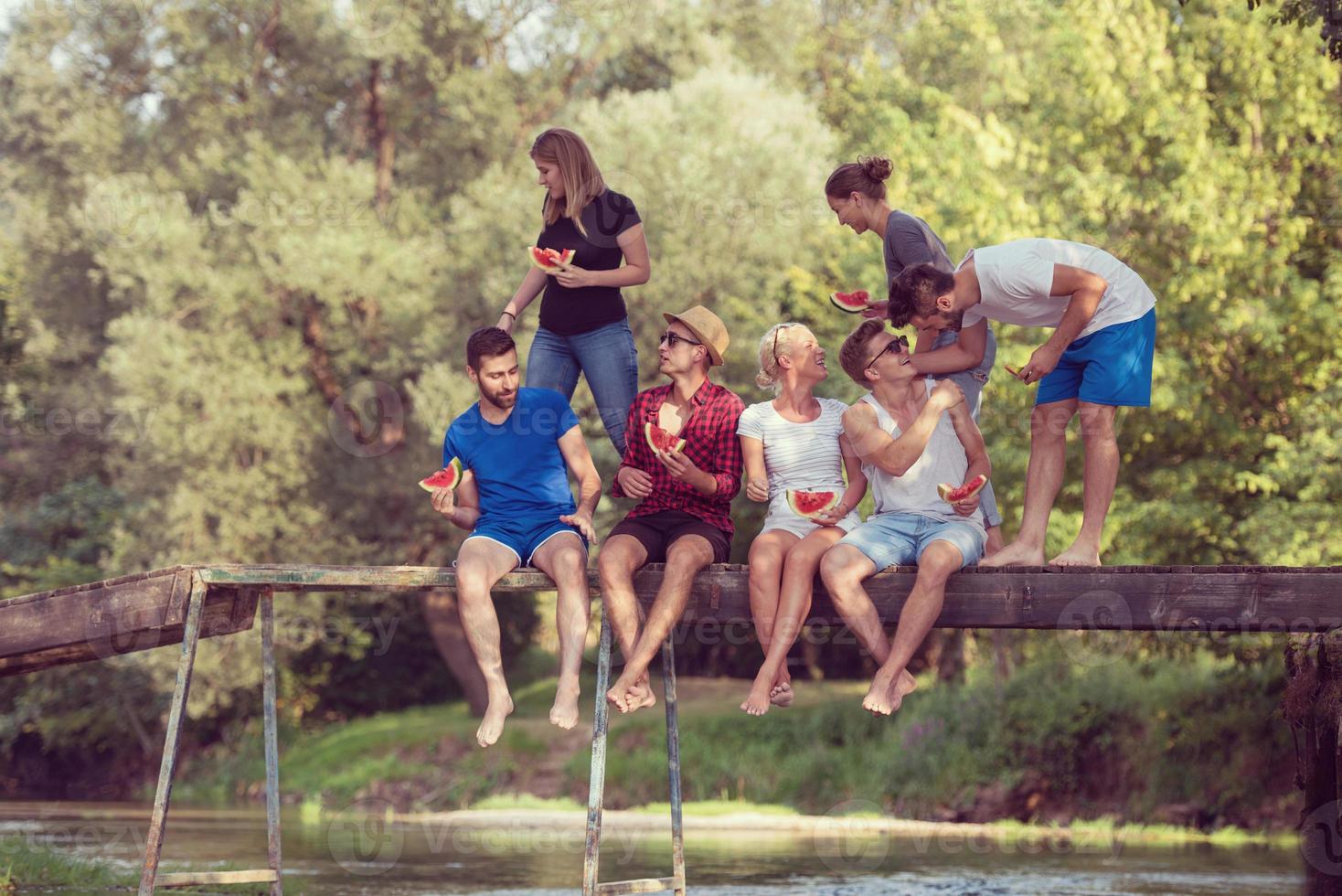 friends enjoying watermelon while sitting on the wooden bridge photo