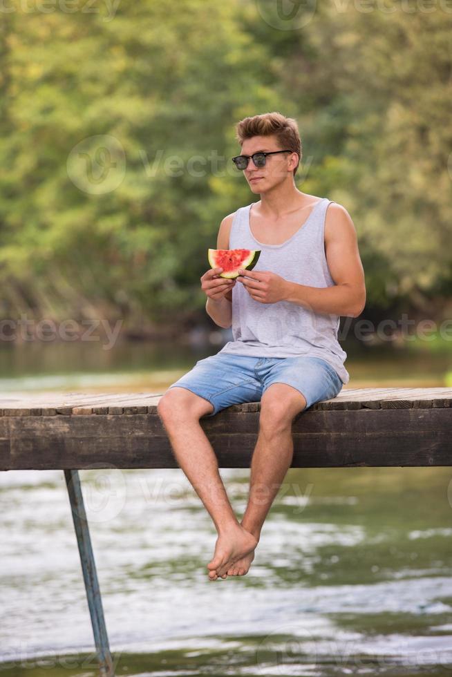 hombre disfrutando de la sandía mientras está sentado en el puente de madera foto