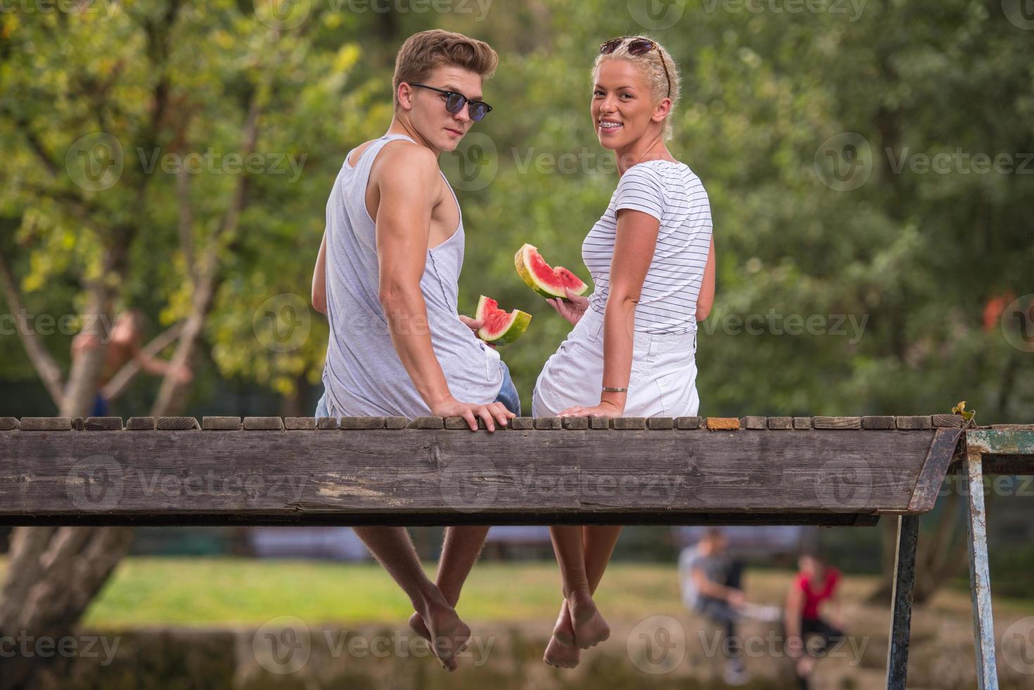 couple enjoying watermelon while sitting on the wooden bridge photo