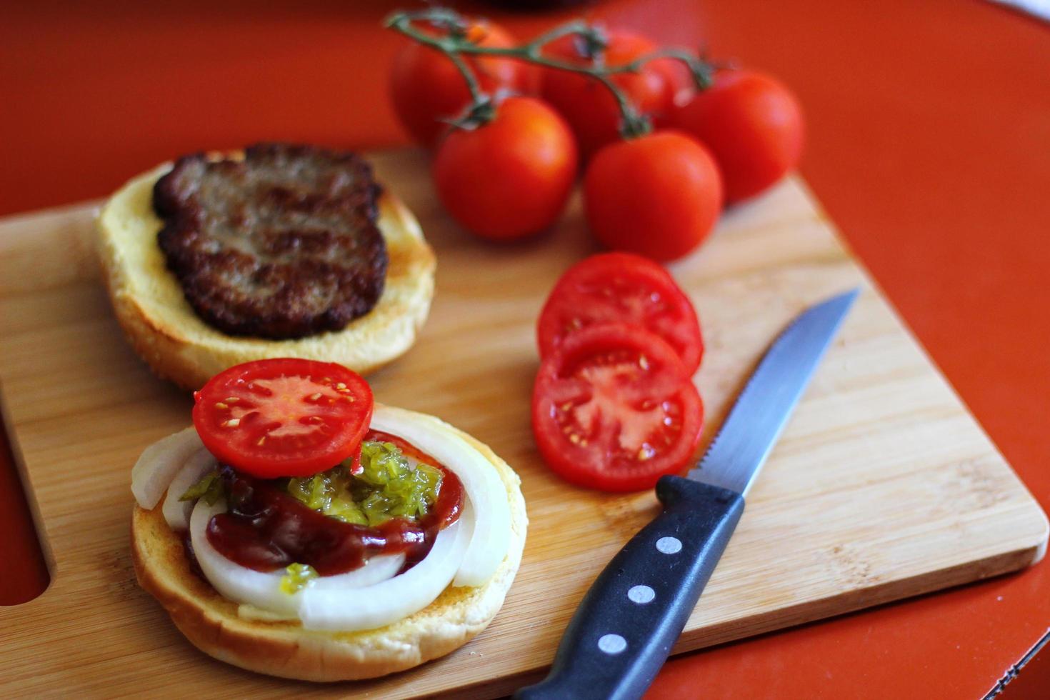 The hamburger is being prepared and served with sliced tomatoes, onions, pickles. on a wooden cutting board in the kitchen photo