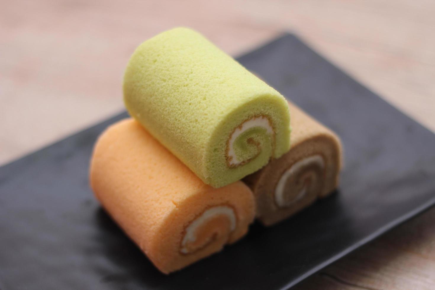 3 Swiss rolls served in a black plate placed on a wooden table. photo