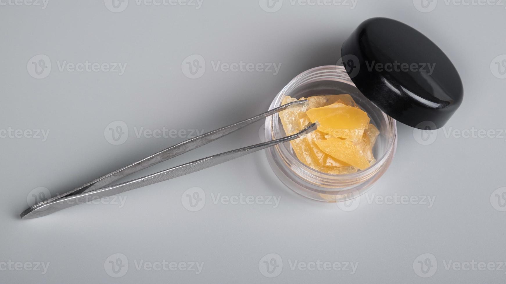 high thc cannabis concentrate,tweezers and container with piece wax extract on gray background photo
