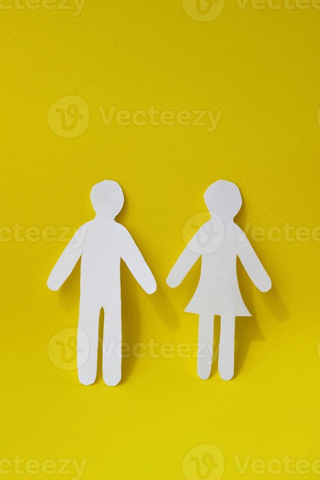 Silhouettes of a man and a woman are carved from white paper, standing side by side on a yellow background. The concept of love, relationships, family. Vertical photo
