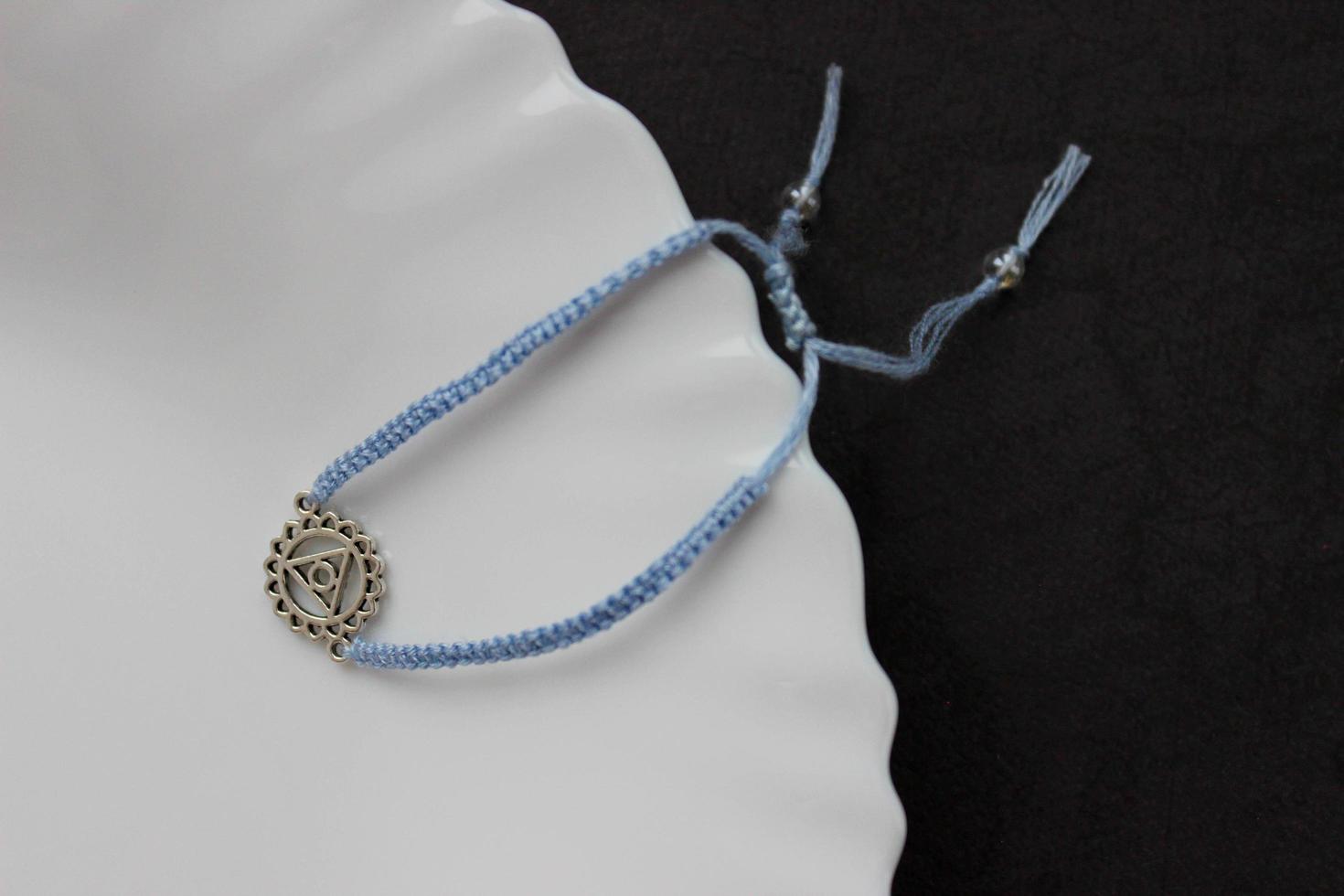 Light blue handmade braded bracelet with chakra vishuddha on the edge of a snow-white plate photo